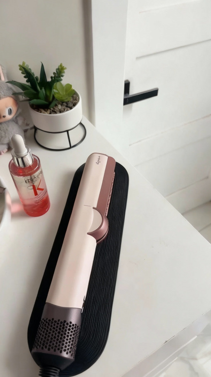Hair straightener on a white surface with a plant and bottle in the background